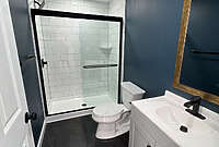 wooden_basement_bathroom remodel bathroom remodel in basement with navy blue walls, black flooring, back hardware and white subway vinyl shower
