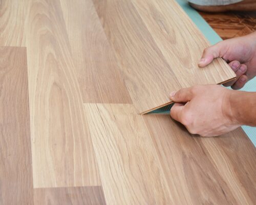 flooring a male's hands laying wooden waterproof flooring in a light wooden color