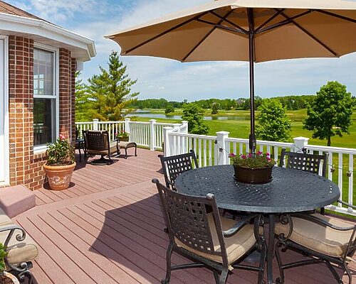 deck off the back of a brick house with a round table and umbrella in the summer