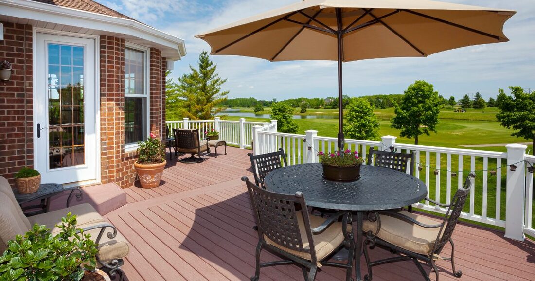deck off the back of a brick house with a round table and umbrella in the summer